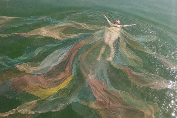 Eine Frau im Wasser umgeben von pastellfarbenen Tüchern, die aussehen wie ein Blanket Octopus